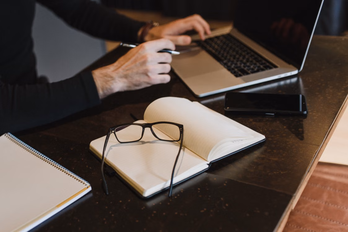 Handen op een laptop naast een notitieboek